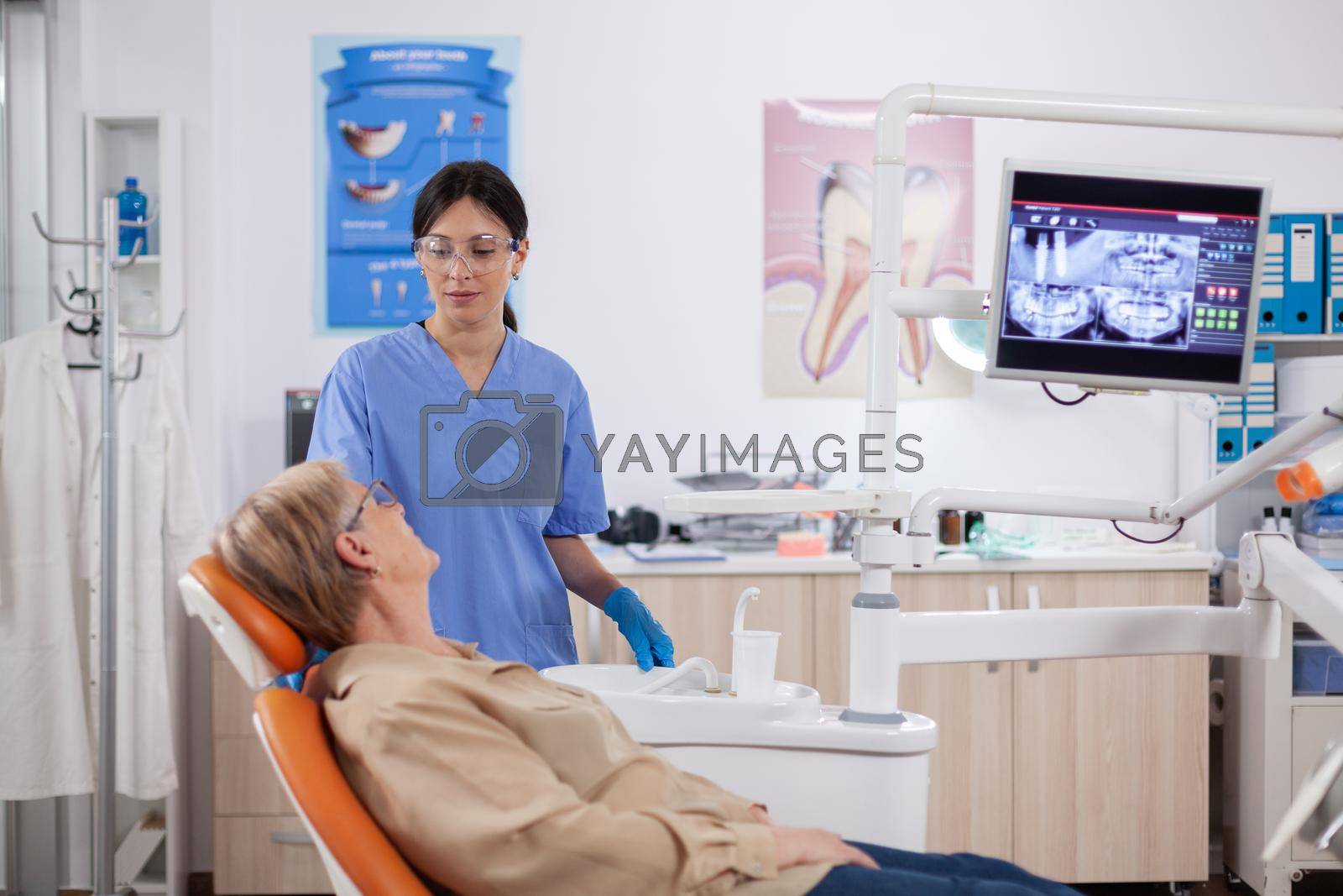 Assistant in dental clinic questioning elderly patient about tooth problems. Senior woman talking with medical nurse in stomatology office about teeth problem.