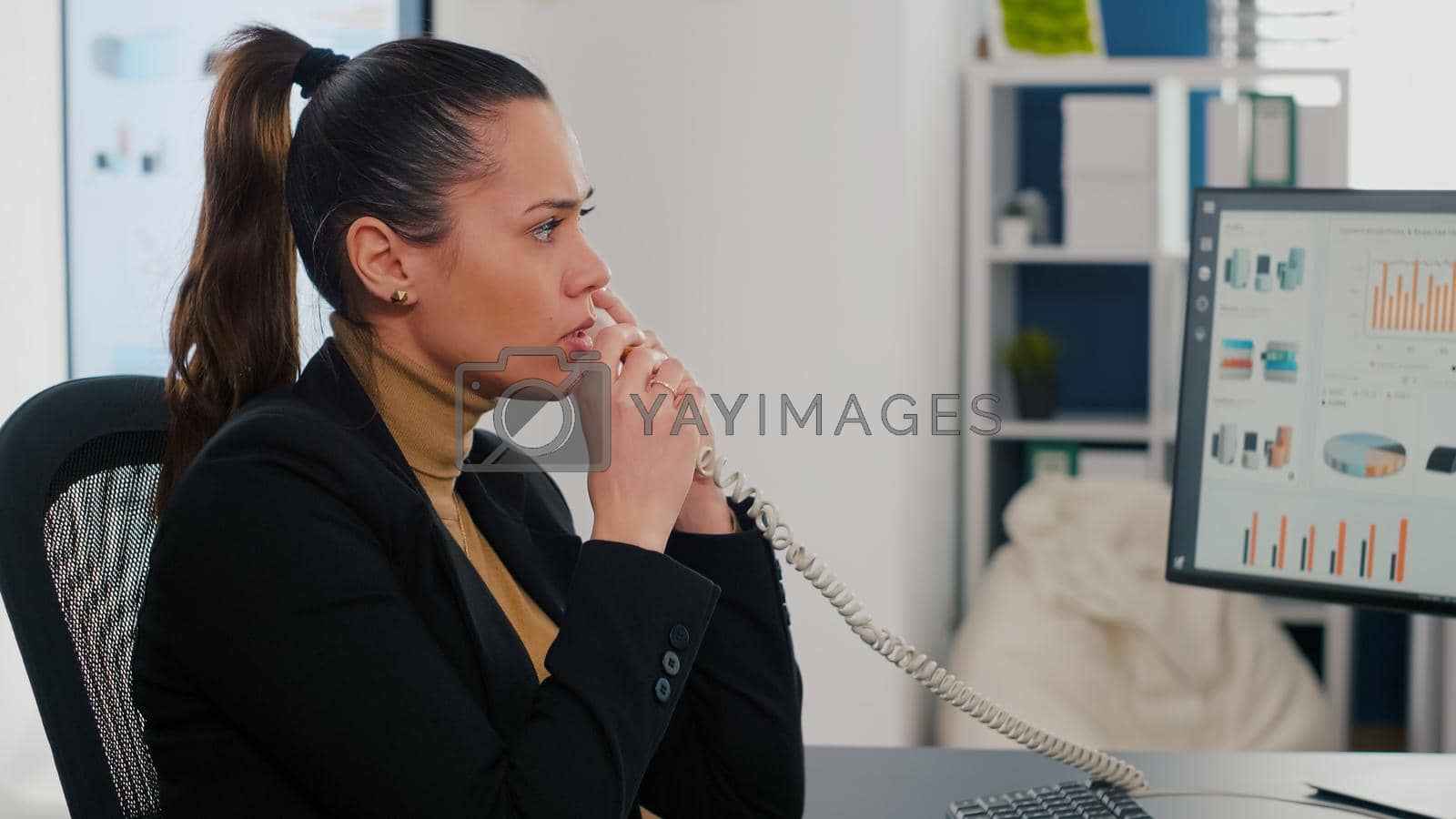 Royalty free image of Multitasking executive manager talking at landline explaining company graphs to remote collegue by DCStudio