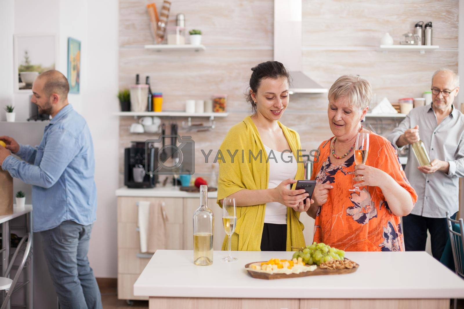 Mother and daughter smiling in kitchen using smarthphone drinking wine.
