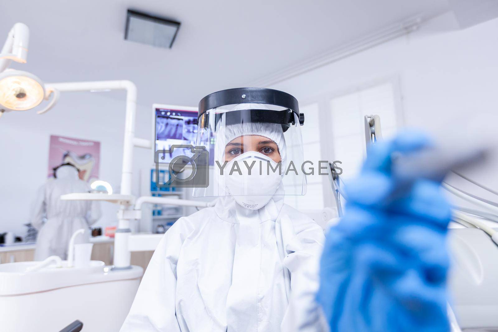 Patient pov of dentist in dental office treating tooth dressed in professional protective gear for covid 19. Stomatolog wearing safety gear against coronavirus during heatlhcare check of patient.