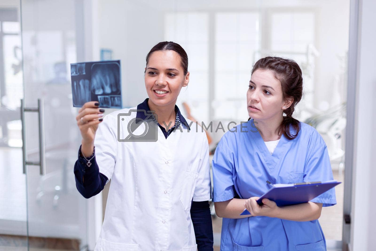 Dentist doctor holding teeth x-ray and nurse taking notes on clipboard in stomatology office. Stomatolog and her assistant in reception of dental clinic looking at teeth radiography.