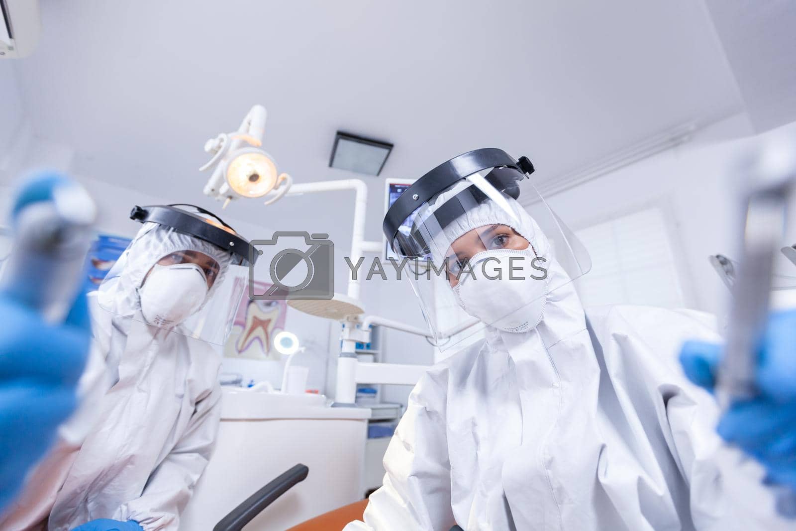 Pov of patient in dental office getting treatment from dentist team lead over to work on teeth cavity. Stomatology team wearing safety equipment against coronavirus treating patient.