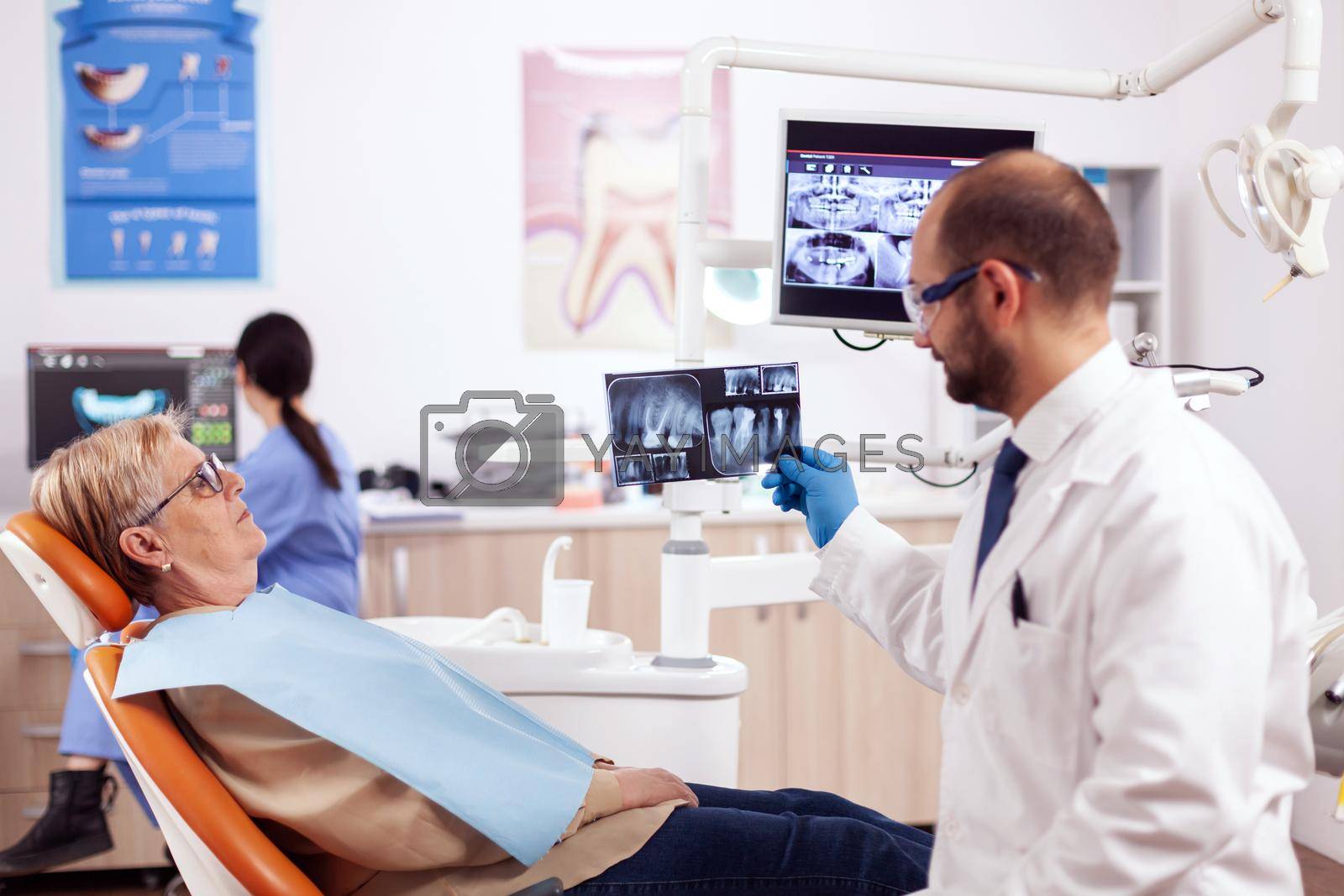 Dentist looking and examining at senior woman dental radiography for treatment. Medical teeth care taker holding patient x-ray sitting on chair during consultation.