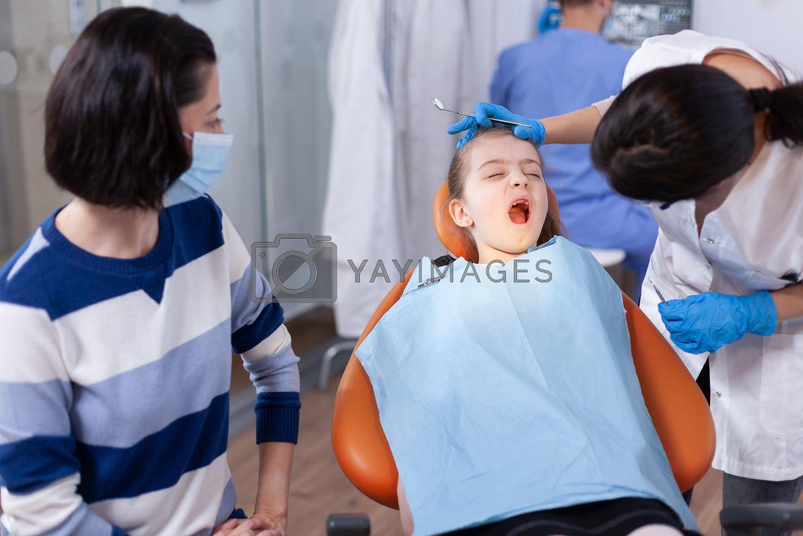 Dental doctor checking tooth hygine of kid with open mouth sitting on chair. Dentistry specialist during child cavity consultation in stomatology office using modern technology.