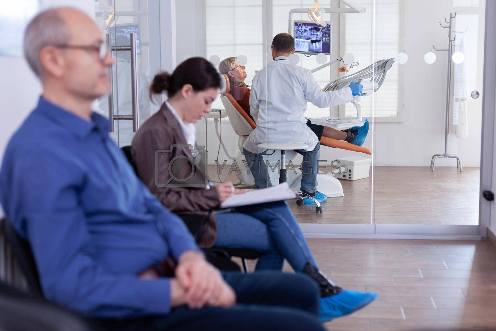 Senior woman sitting on chair in dental office listening dentist talking about diagnosis for teeth cavity looking at digital x-ray radiography. Patients filling form in waiting area.