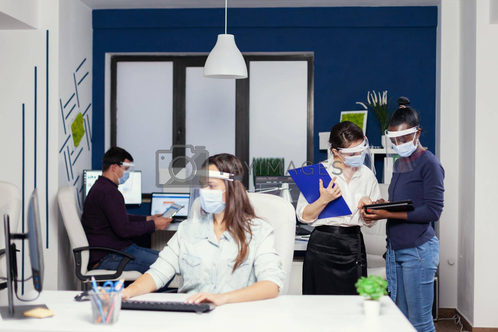 Business people planing financial strategy in workplace wearing face mask for covid19. Multiethnic business team working respecting social distance during global pandemic with coronavirus.