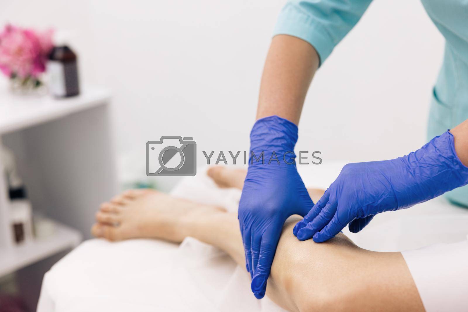 Royalty free image of Physiotherapist worker woman assisting physical medical exercise recovery after injuries. Doctor in gloves examining painful knee of female patient leg trauma. Healthcare medical insurance concept by uflypro