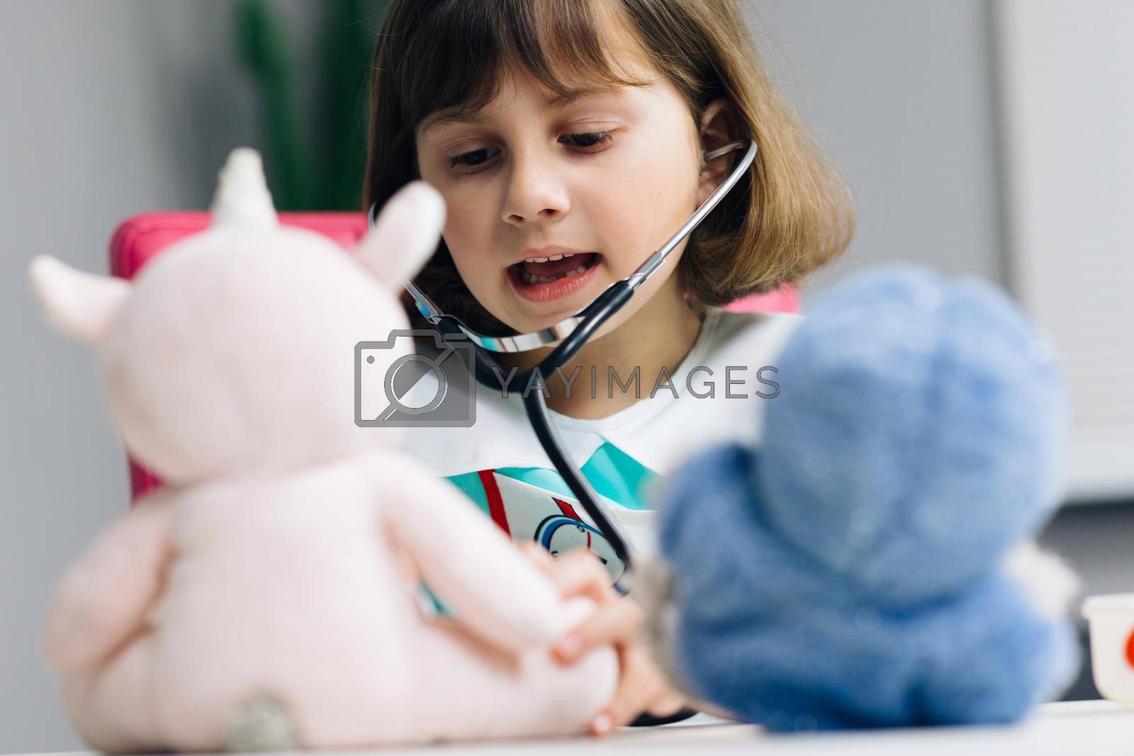 Cute preschool girl kid wearing medical uniform, listening to pets breathing, parrots and toy patients. Child playing hospital game pretending to be doctor, veterinarian, doctor treat homeless animals