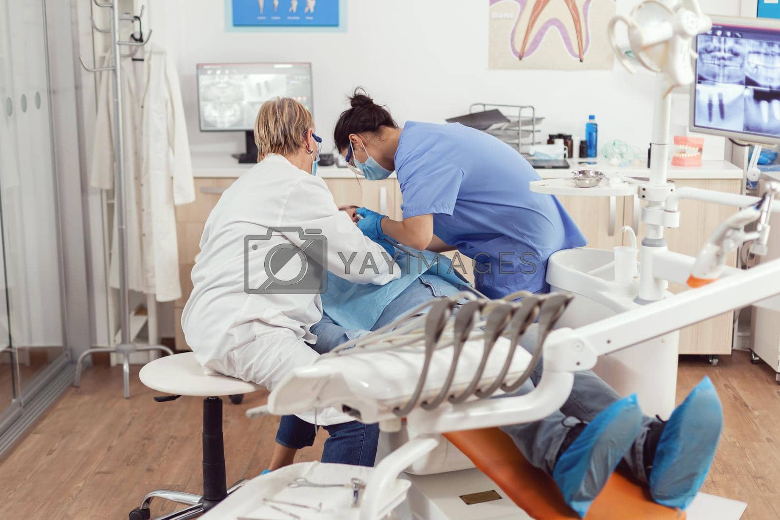 Sick man sitting on dental chair during medical examination while senior dentist woman doing oral surgery in dentistry office. Hospital team examining patient toothache preparing tooth treatment