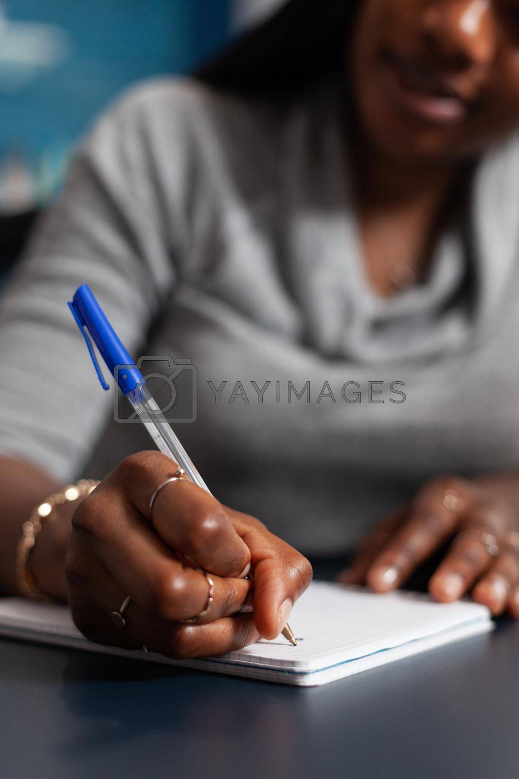 Closeup of black student hands writing university homework during online communication lesson studying business education. African american woman working remote from home in living room