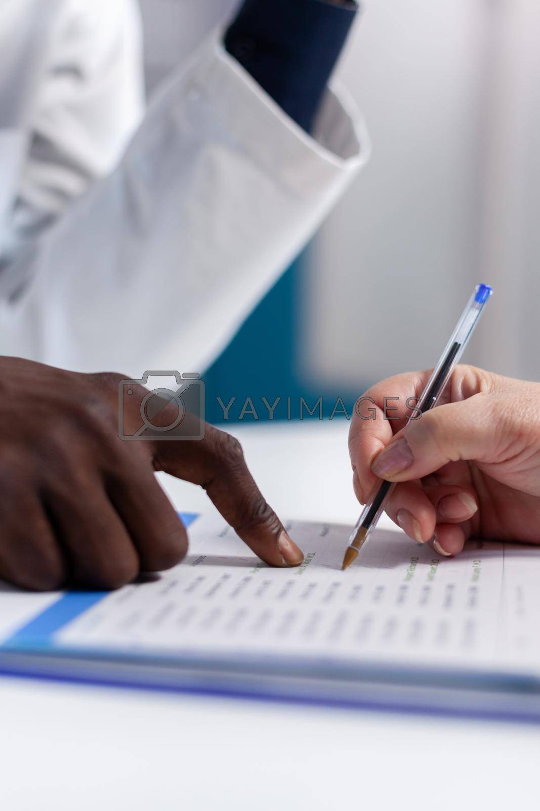 Close up of hands on desk at healthcare clinic. Caucasian patient holding pen and signing document file for appointment checkup while african american doctor showing information