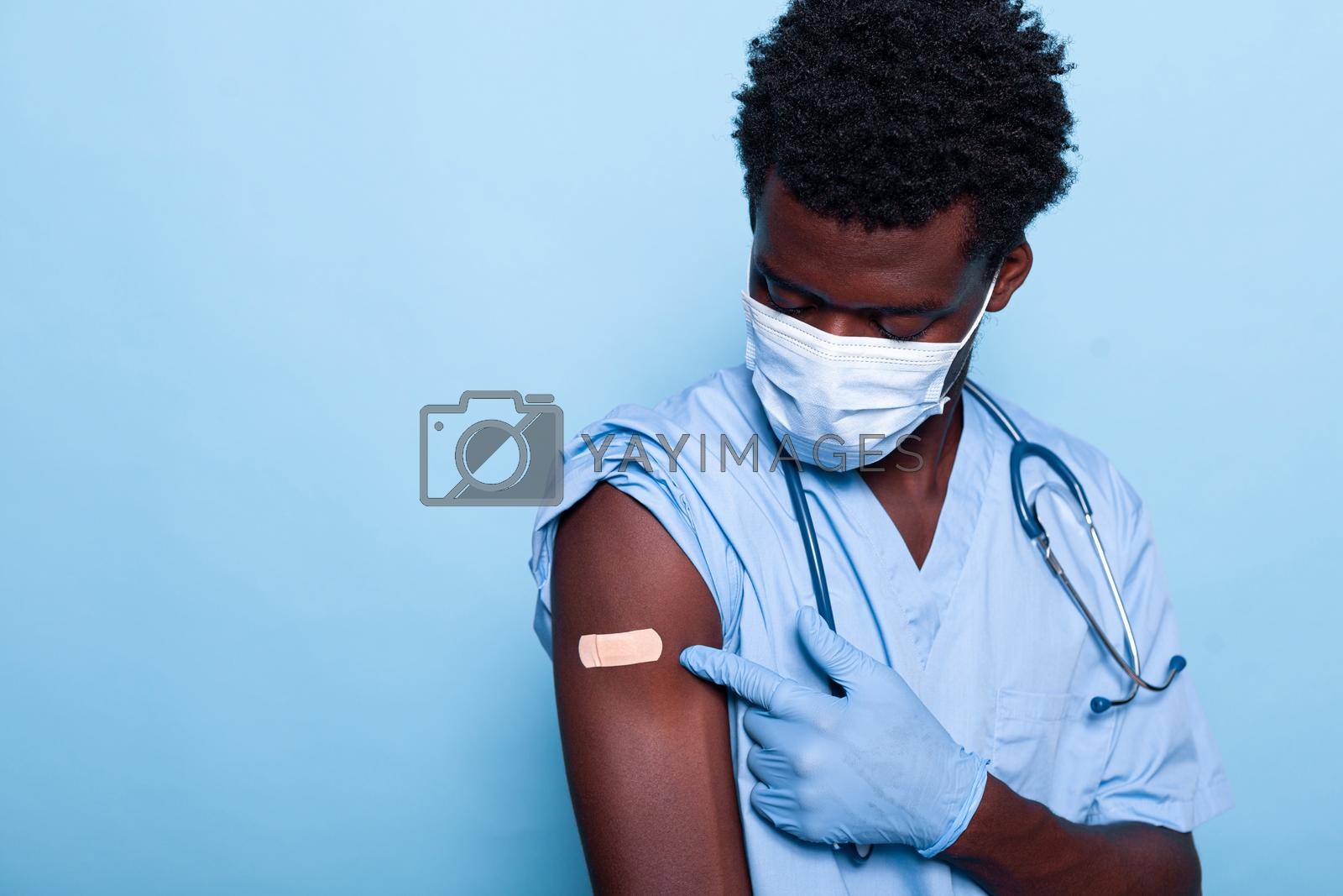 Healthcare specialist having adhesive bandage after vaccination against coronavirus. Vaccinated nurse with uniform and face mask pointing at vaccine shot patch for immunity and prevention