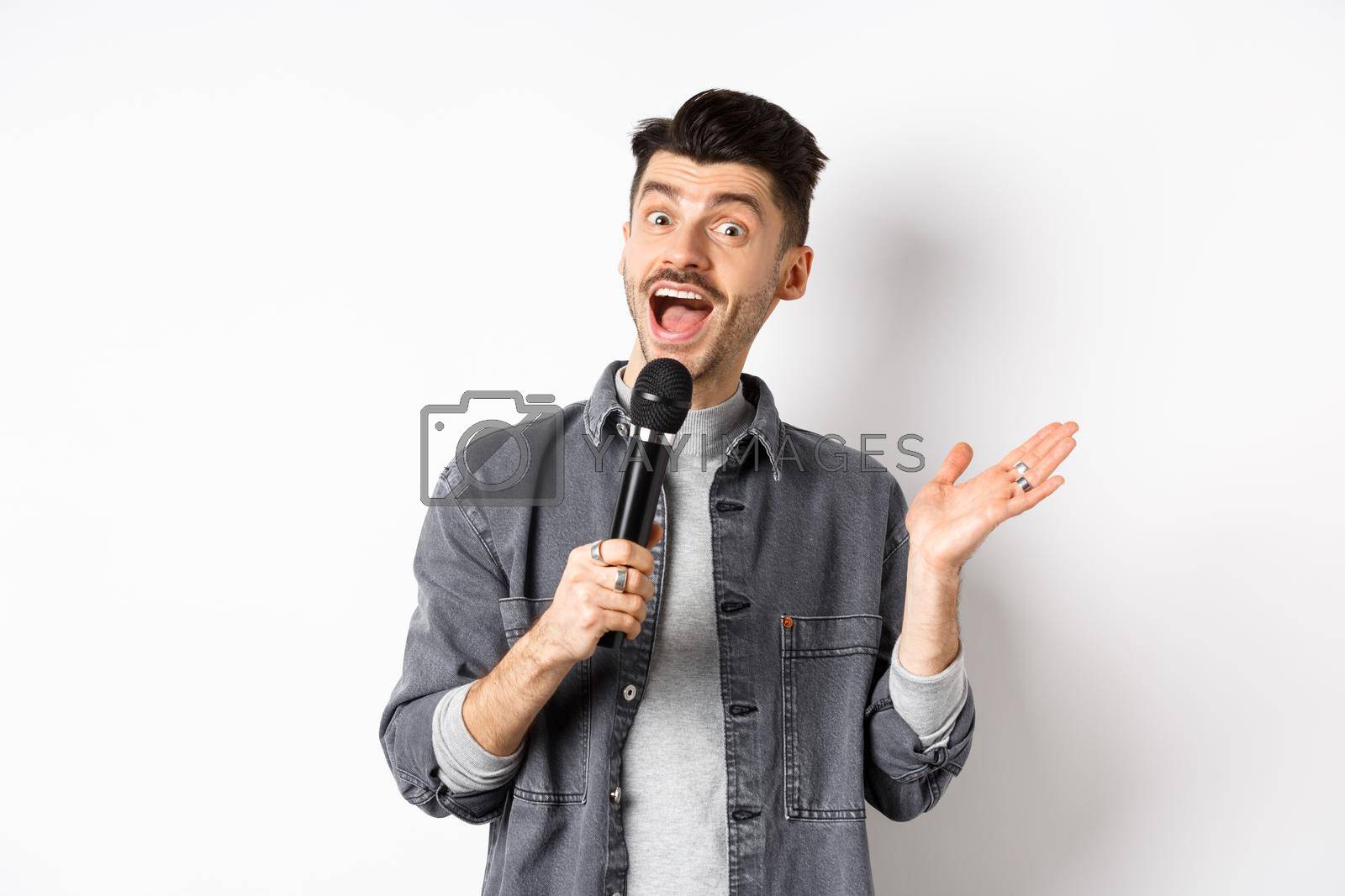 Royalty free image of Excited stylish guy giving speech, talking in microphone, perform or sing karaoke, standing on white background by Benzoix