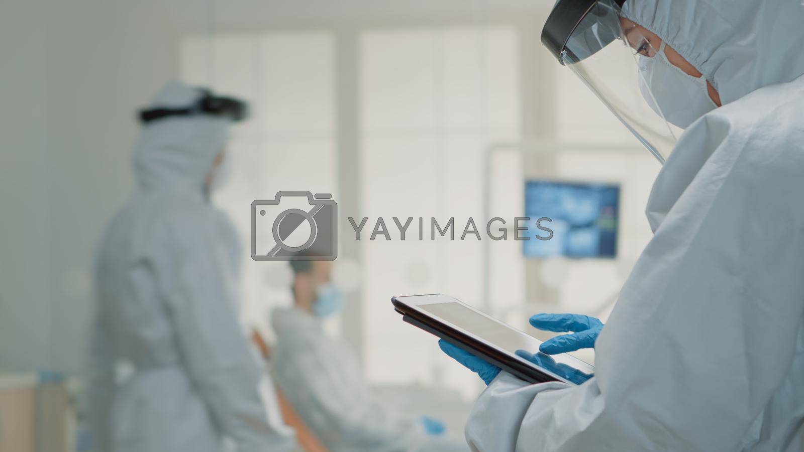 Dental assistant examining teeth x ray on digital device at oral healthcare clinic while dentist consulting patient in background. Orthodontist team working with technology for modern hygiene