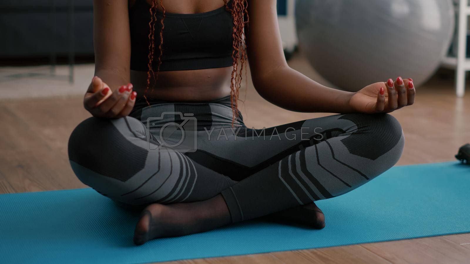 Flexible fit black woman practicing respiratory exercise during morning fitness sport workout in living room sitting on yoga map. Athlete adult stretching body muscles enjoying healty lifestyles