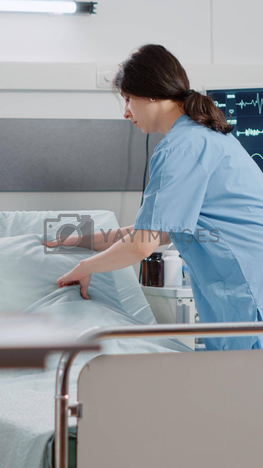 Woman nurse making bed in hospital ward for healthcare treatment and recovery. Medical assistant preparing reanimation room with oxygen tube and heart rate monitor for patient.