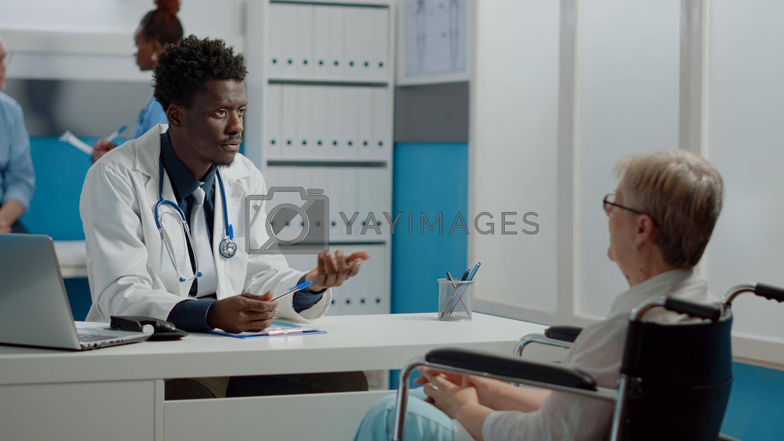 Invalid patient with disability having healthcare appointment with doctor in medical cabinet at facility. Medic consulting disabled woman sitting in wheelchair while receiving advice