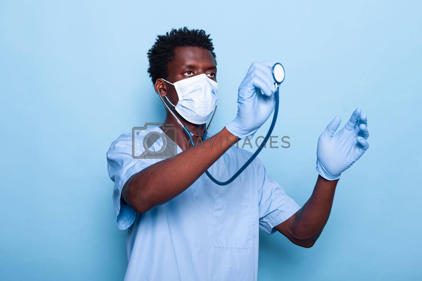 Healthcare nurse holding and using stethoscope for cardiology heartbeat examination. Man cardiologist with medical instrument wearing face mask and gloves against coronavirus pandemic