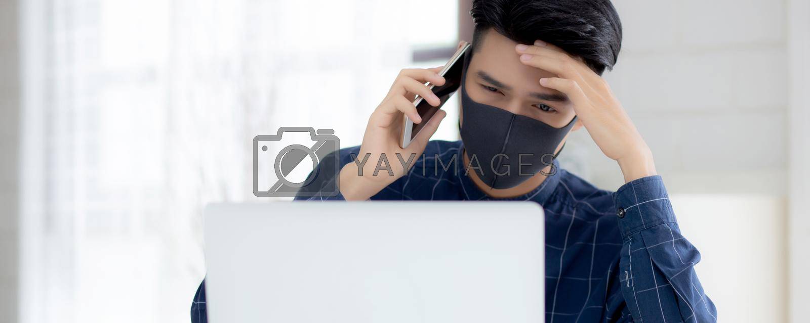 Royalty free image of Young asian business man in face mask talking smartphone and work on laptop computer for protect covid-19, businessman quarantine work from home with notebook, social distancing and stay home. by nnudoo