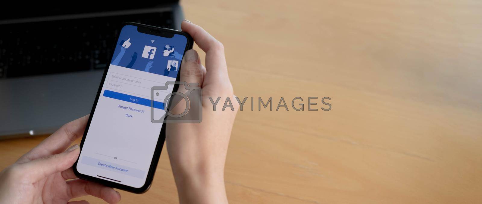 CHIANG MAI ,THAILAND AUG 18 2021 : Woman holding a iPhone X with social Internet service Facebook on the screen...