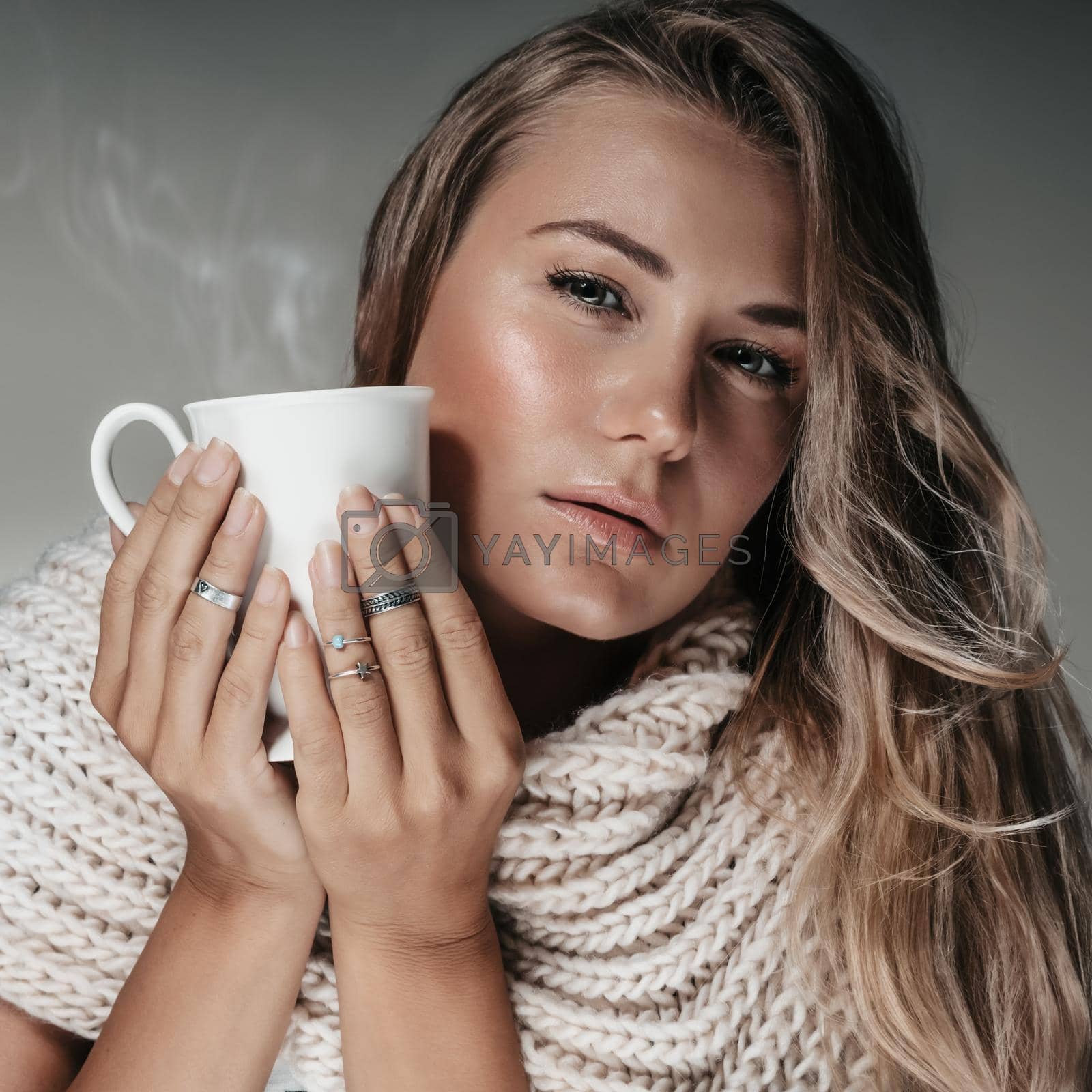 Closeup Portrait of a Beautiful Blond Woman Wearing Big Knitted Scarf Holding Cup of Hot Cappuccino. Fashion Autumn Look.