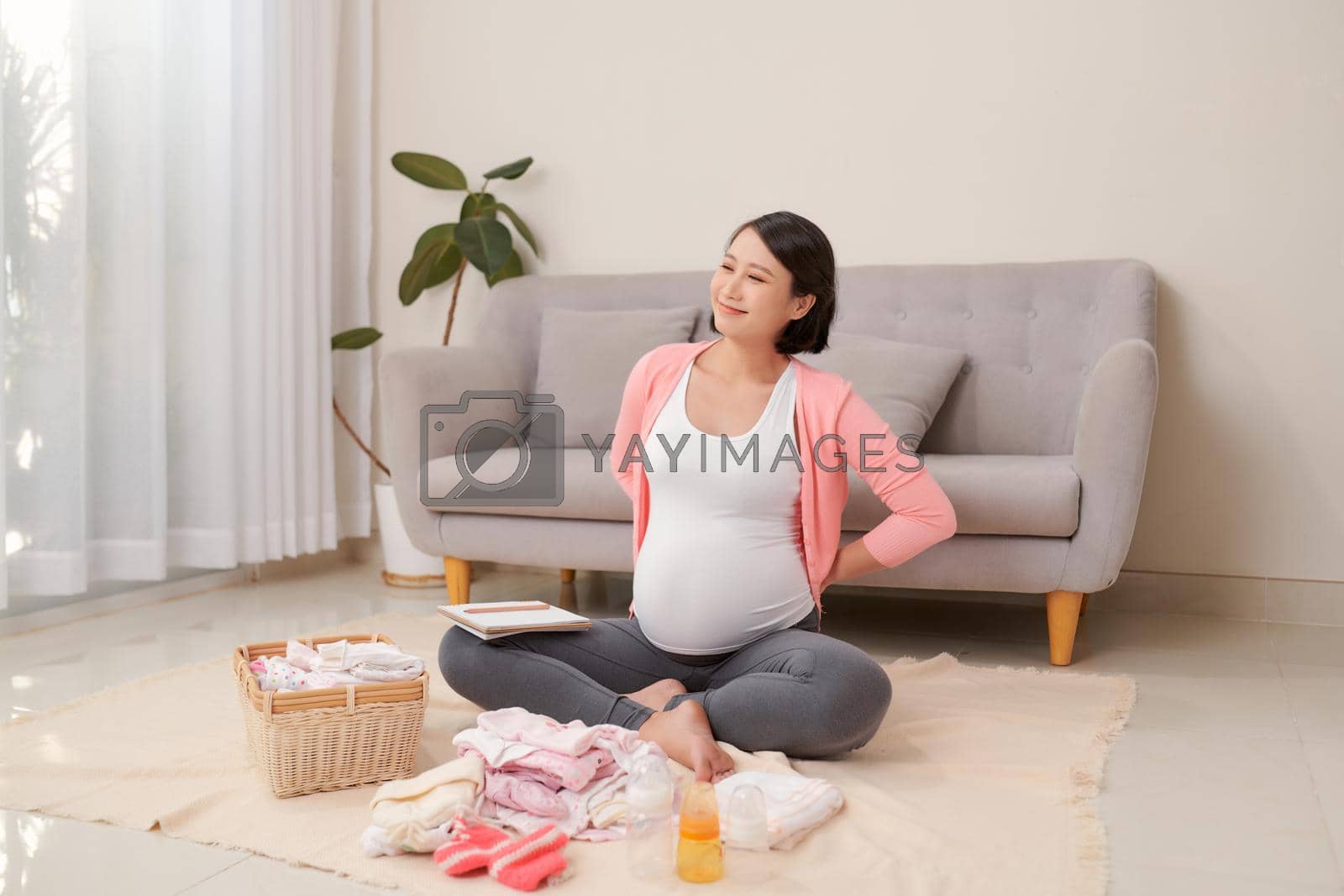 Happy young mother with travel luggage of baby clothes at home
