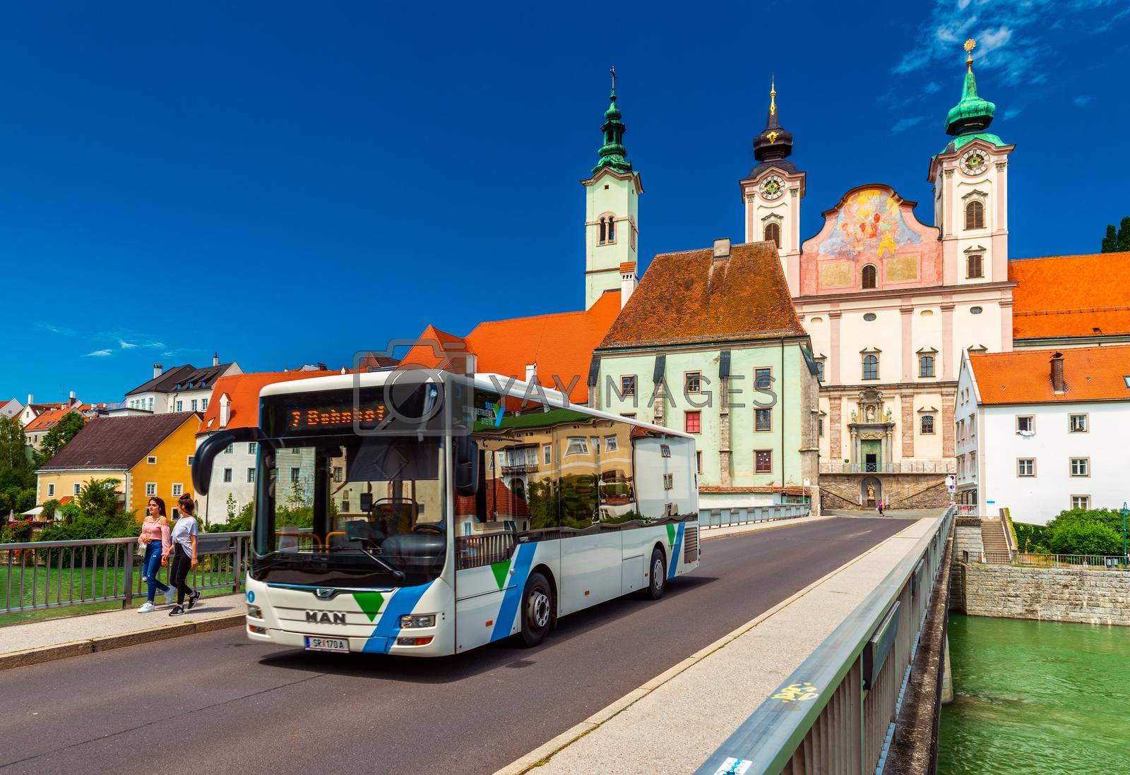 Royalty free image of Steyr - June 2020, Austria: View of the Steyr Bridge with a modern bus, walking girls, and St. Michael's Church behind by travellaggio