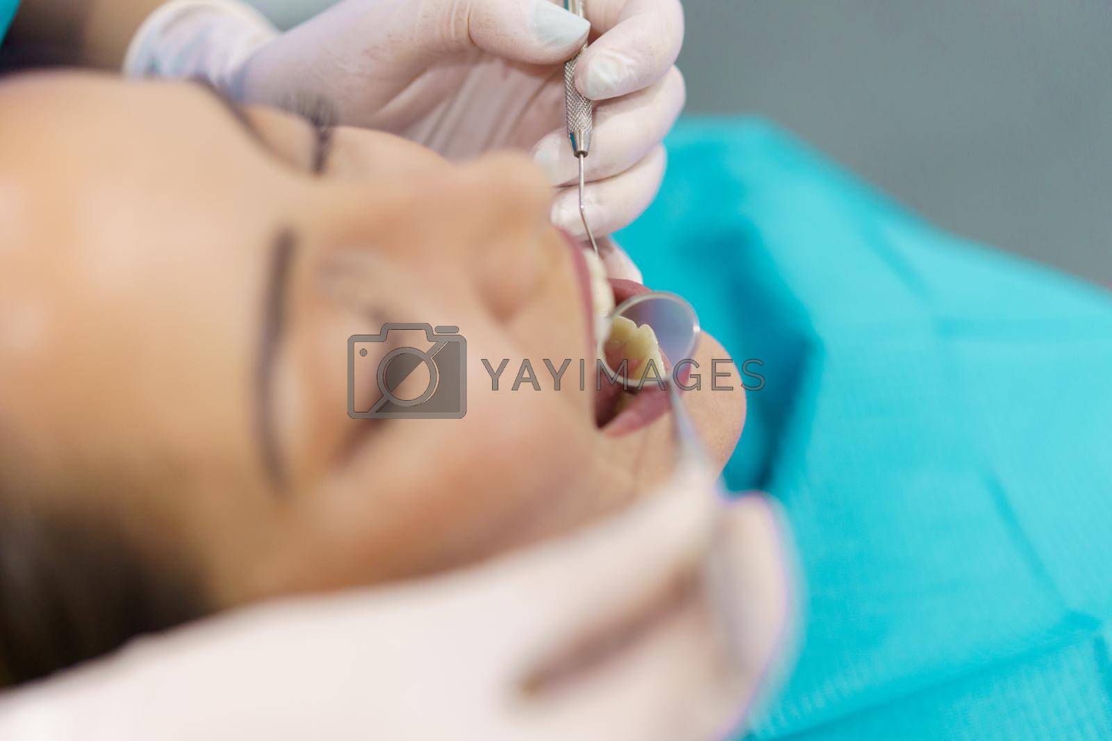 Dentist checking the inside of her female patient's teeth with a dental mirror.