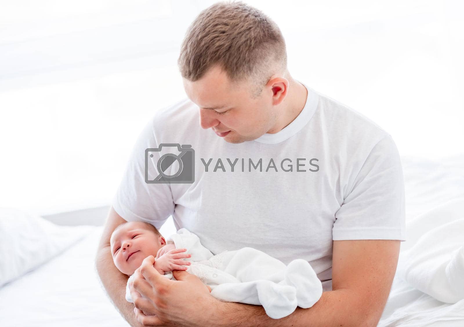Adorable newborn baby girl wearing white costume sleeping in father hands. Cute infant child napping at home and parent dad holding her