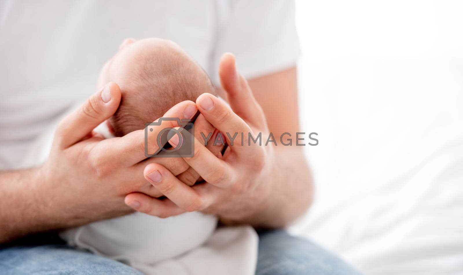Closeup view on father hands holding newborn baby daughter in the bedroom with daylight. Beautiful portrait of dad parent cares about napping infant child