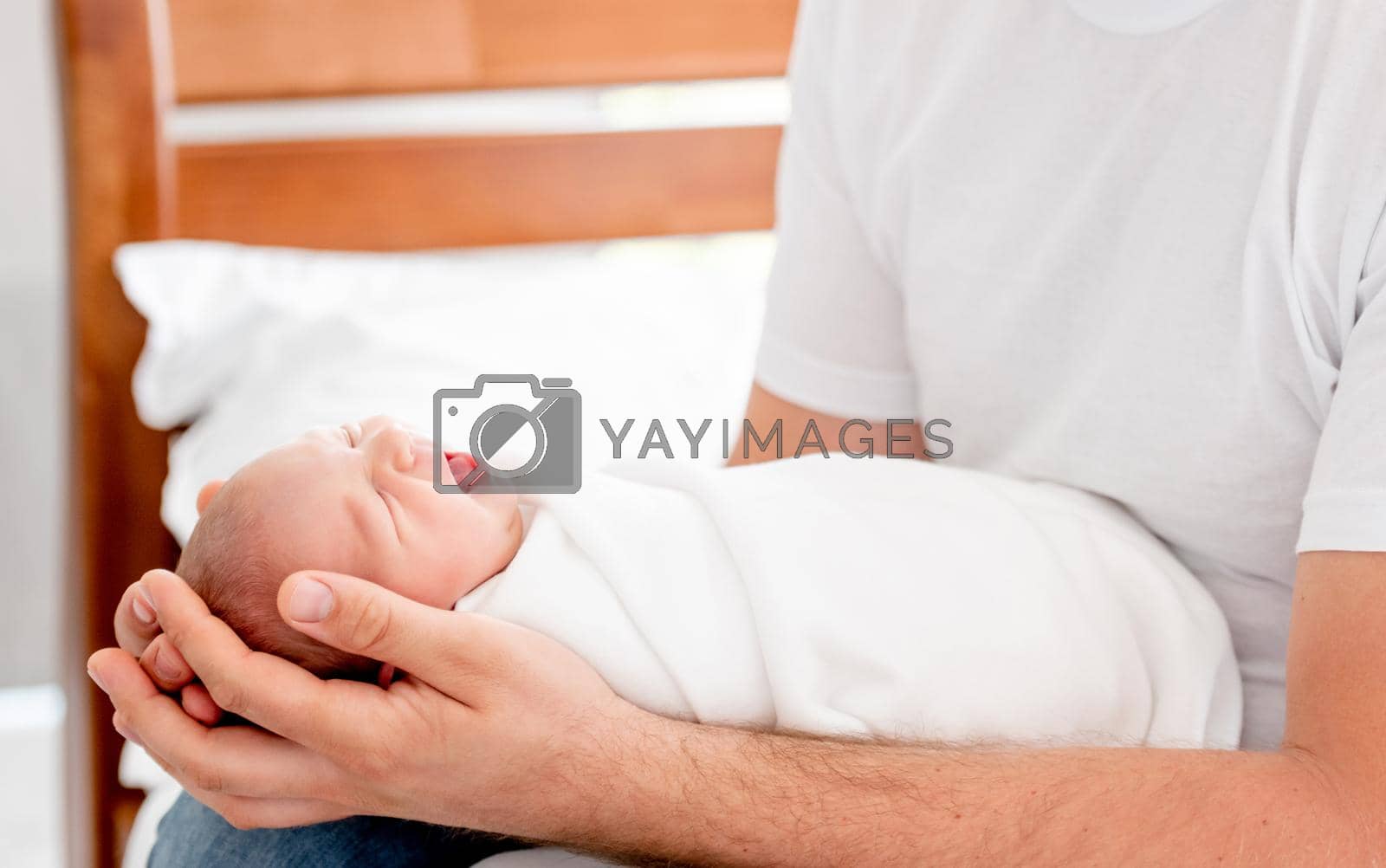Father holding in his hands sleeping newborn baby daughter. Parent dad sitting in the bed with napping infant child at home
