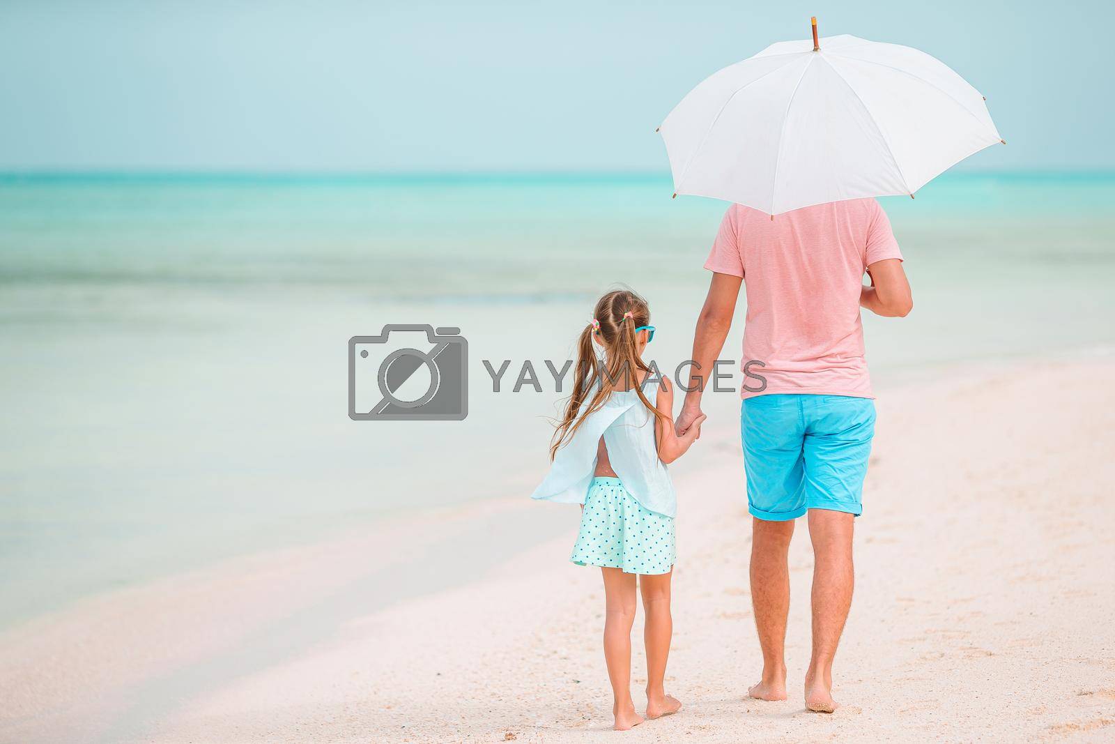 Family of father and little girl on tropical beach with umbrella of the sun