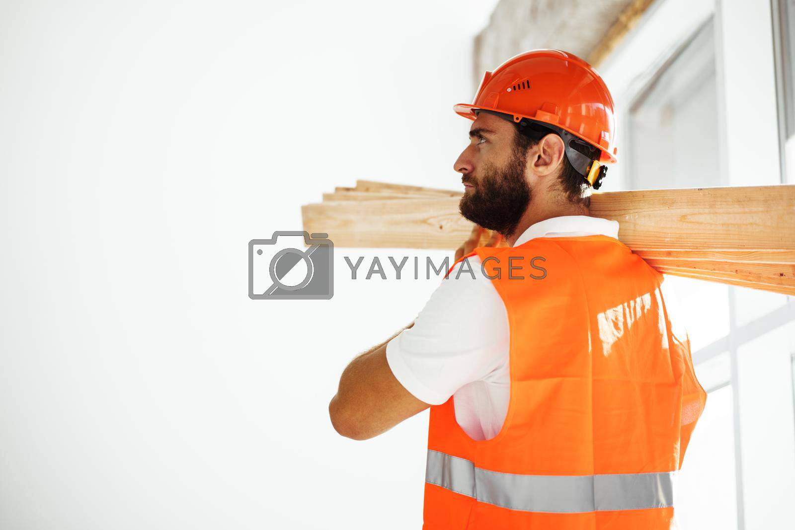Royalty free image of Builder man in hardhat carrying timber on building site, close up . by Fabrikasimf