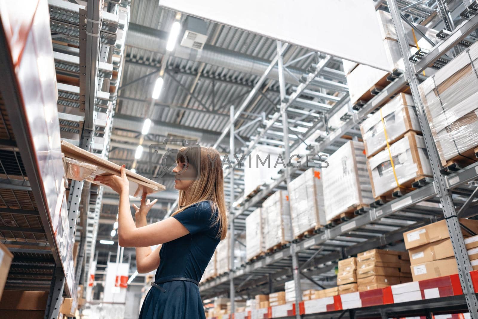Royalty free image of Wholesale warehouse. Beautiful young woman worker of store in shopping center. Girl looking for goods with a tablet is checking inventory levels in a warehouse. Logistics concept by Malkovkosta