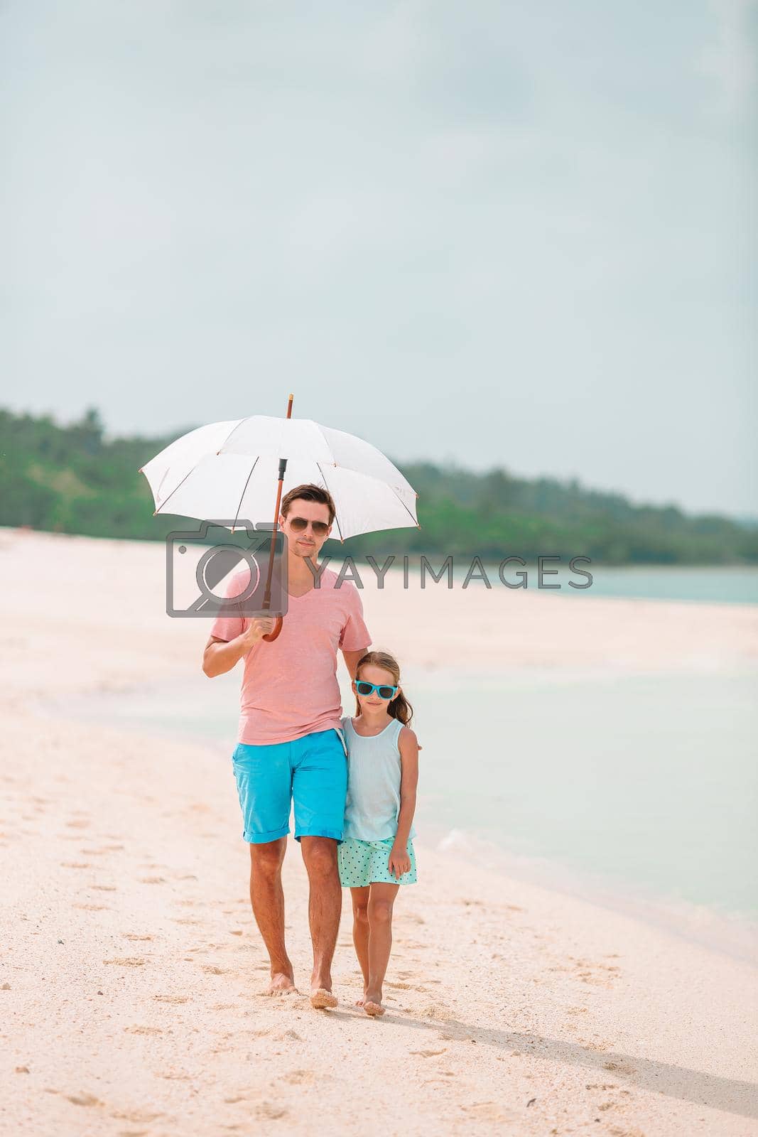 Family of father and little girl on tropical beach with umbrella for the sun
