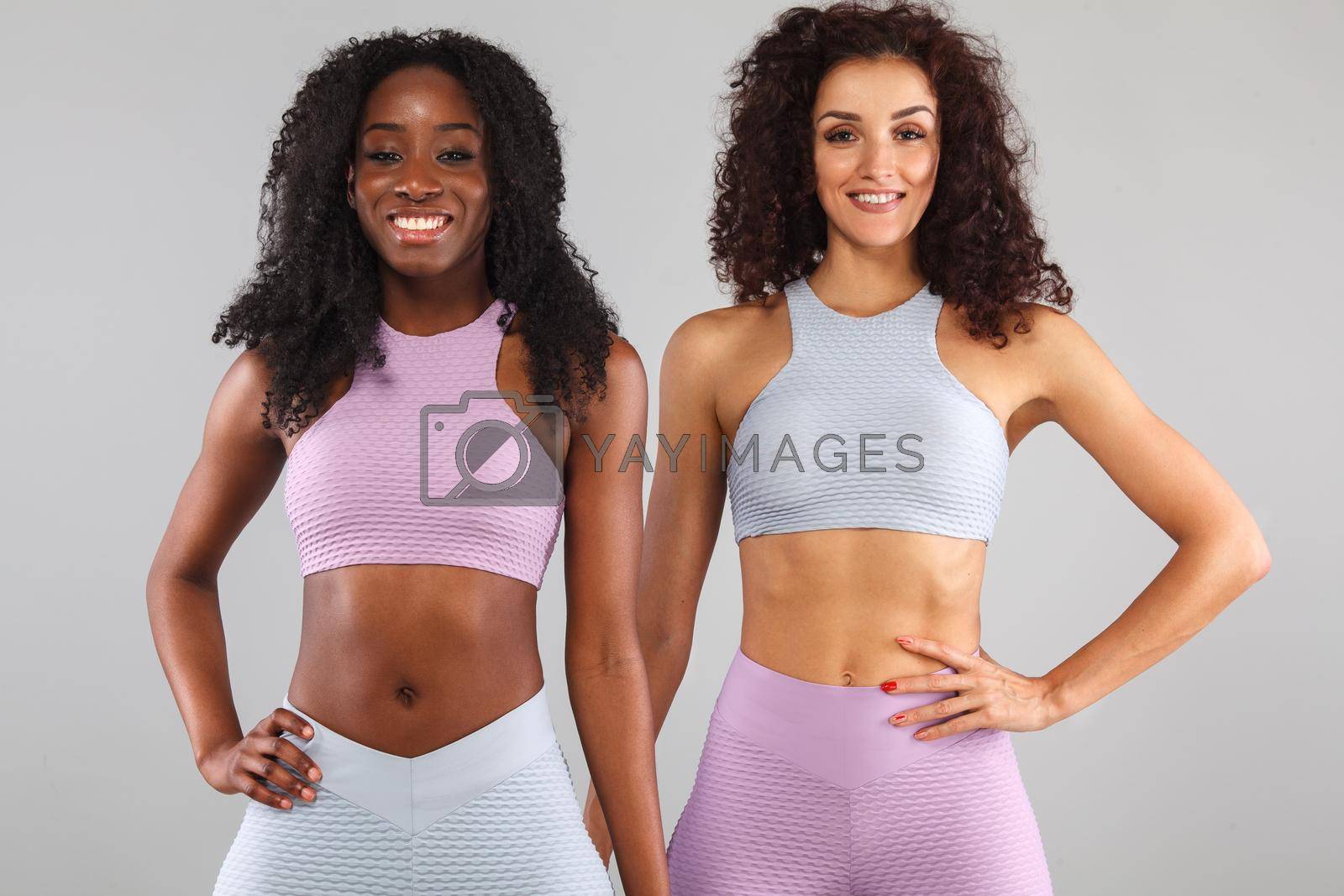 Attractive excited fitness girls in sportwear jumping of joy isolated over light background