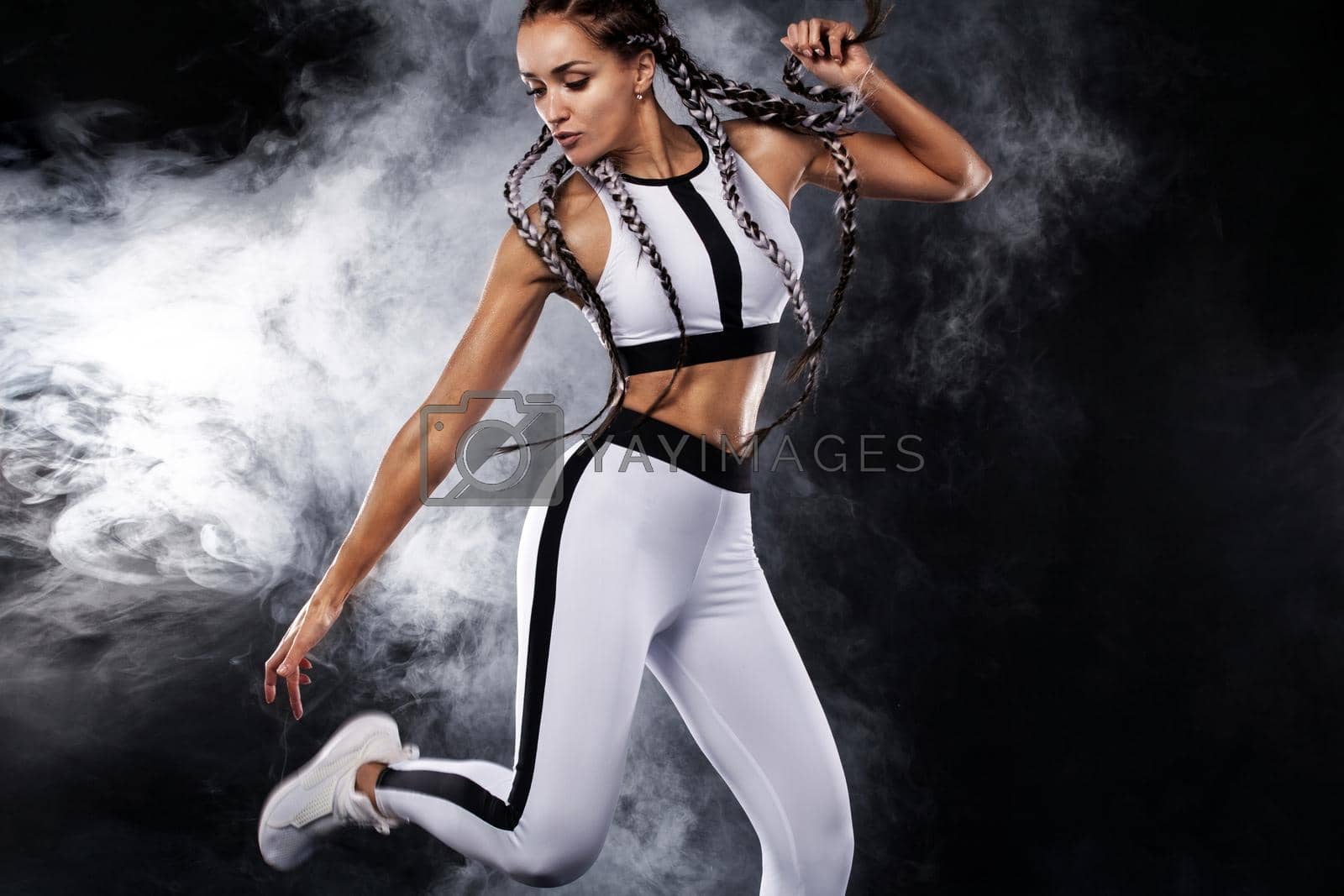 A Strong athletic, female runner on the black bacground wearing a tight, fitness outfit.