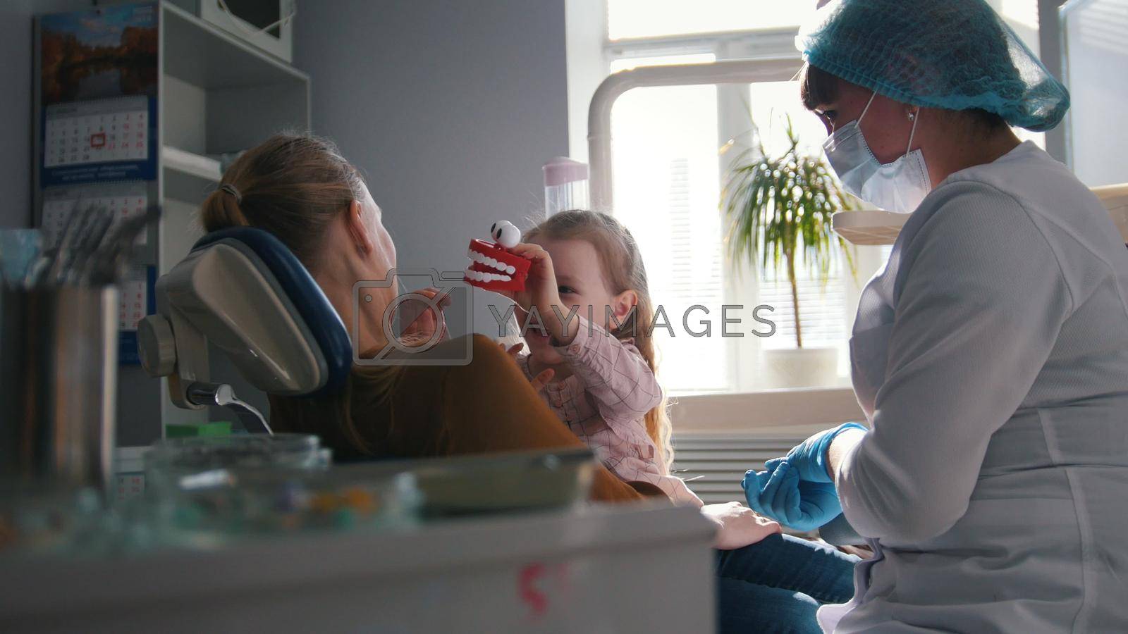 Girl, her mom and the dentist in the dental office, the stomatologist advising with a special toy, health care since childhood