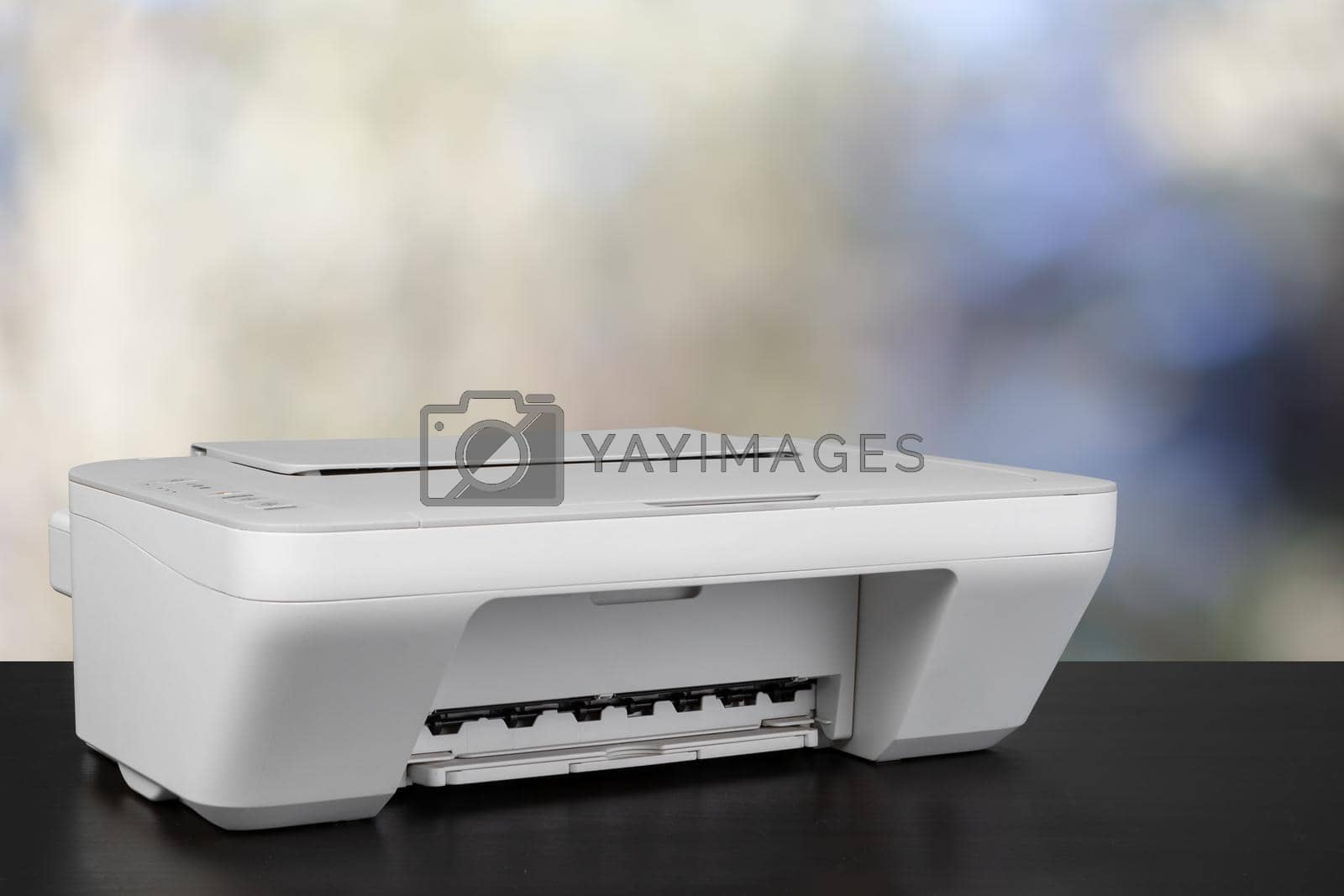 Royalty free image of Compact laser printer on black desk against blurred background by Fabrikasimf