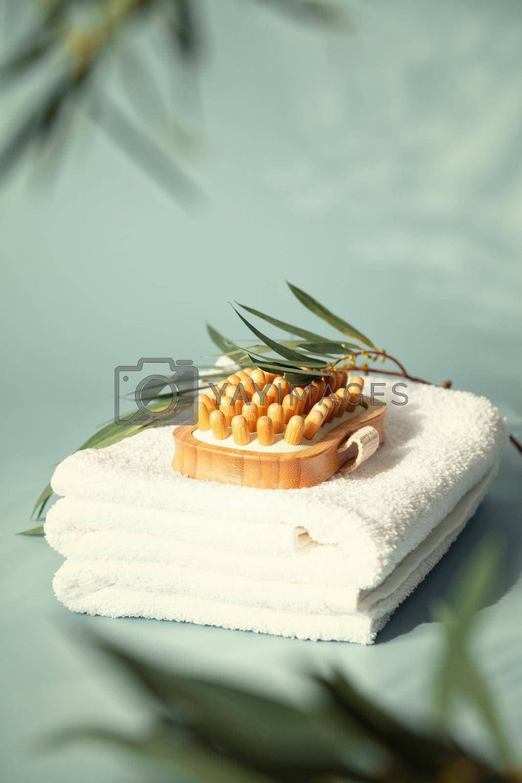 Massage wooden brush on white spa towels with eucalyptus leaves pastel blue background, anti-cellulite massage and body care concept
