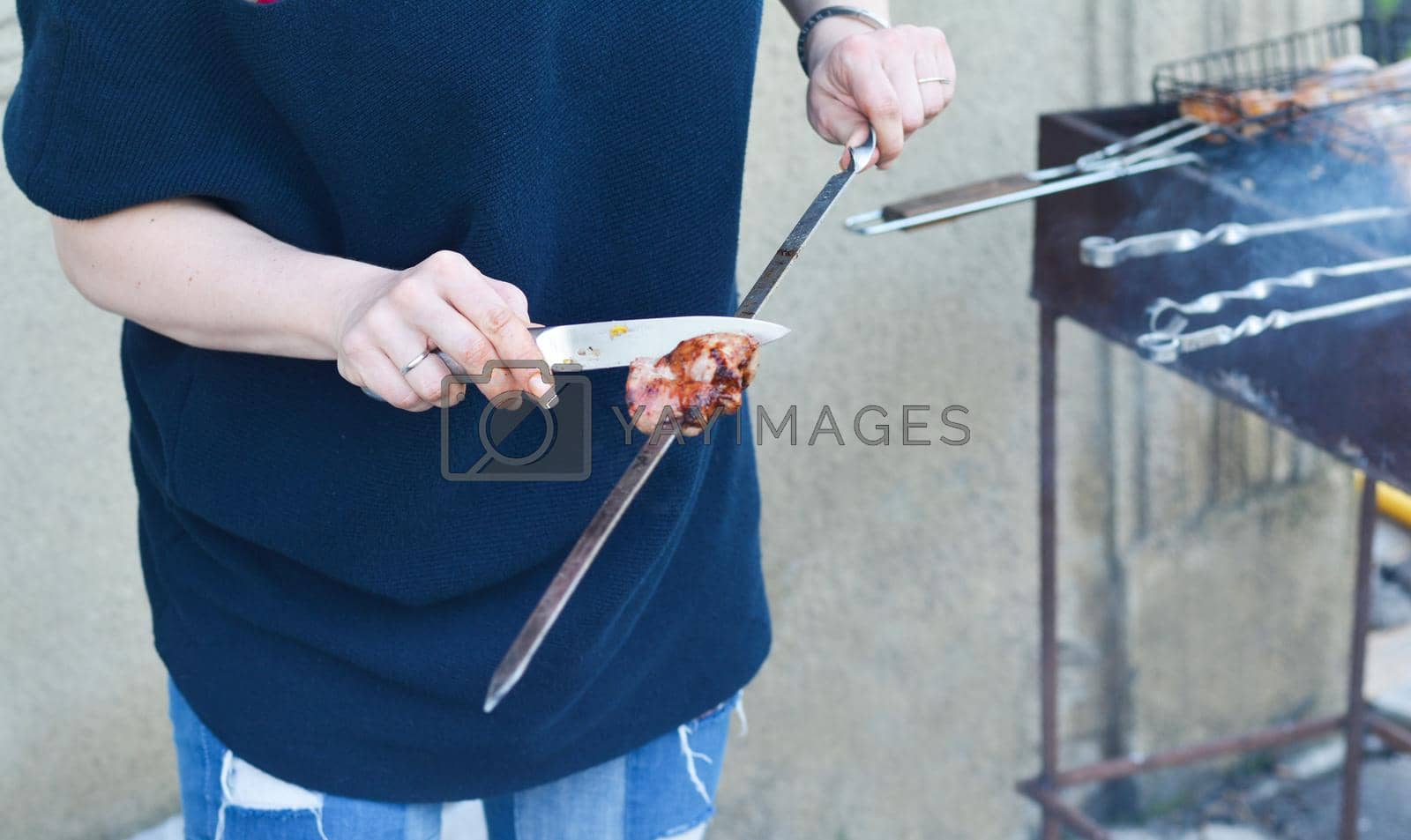 Royalty free image of Women's hands cut barbecue meat Skewer on the grill by Godi