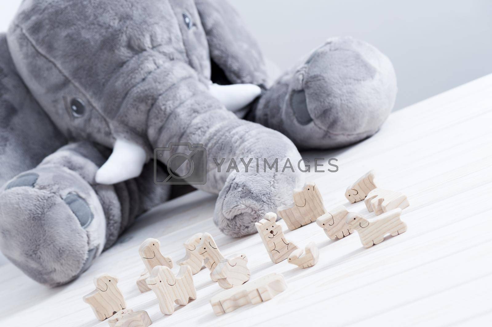 cute wooden toy animals on white wood plank with giant elephant doll in the background