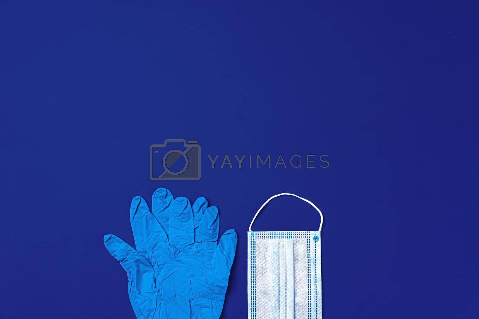 Royalty free image of Medical gloves and surgical protective face mask on dark blue background by Fabrikasimf