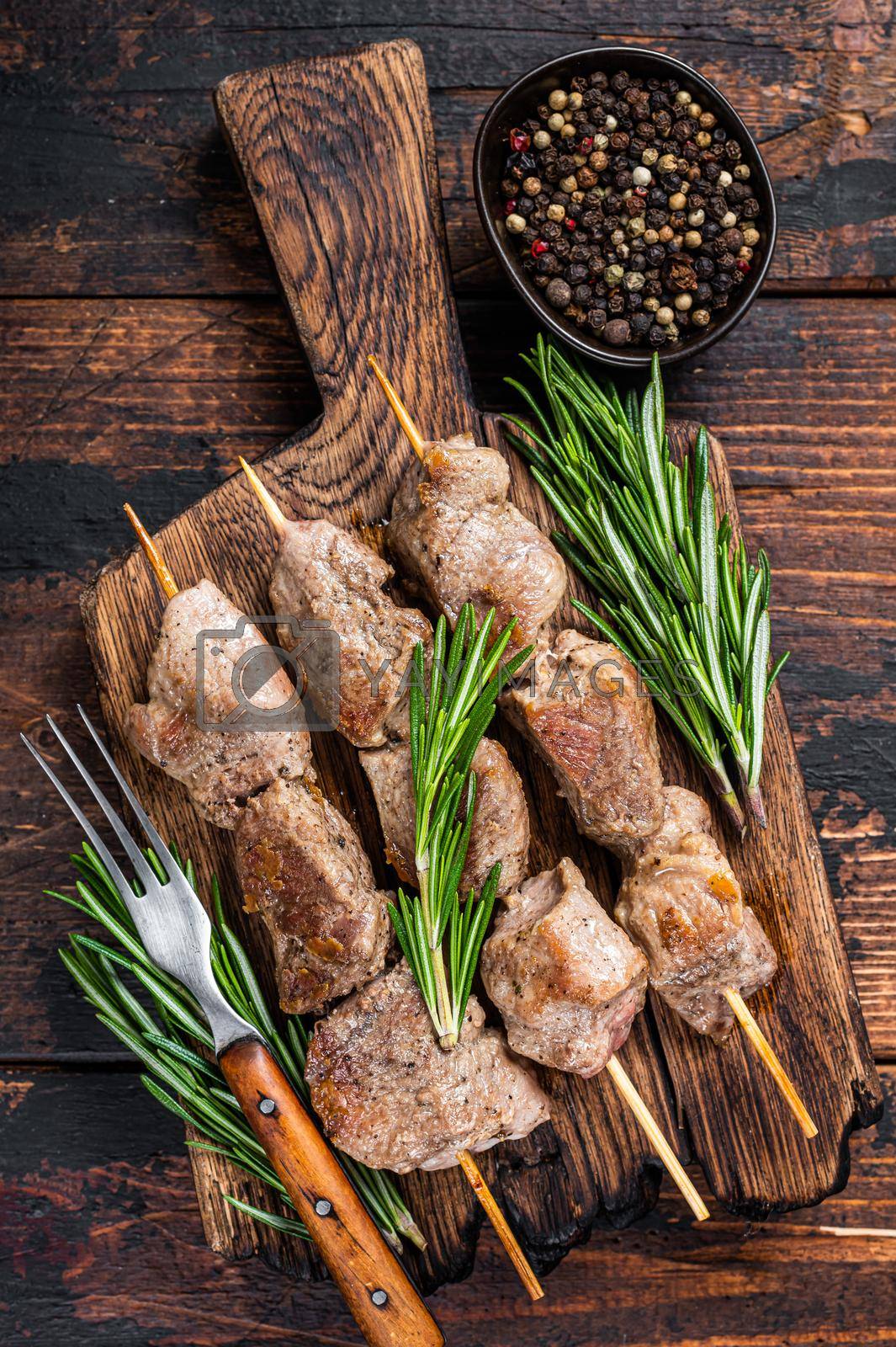 Royalty free image of Pork meat Shish kebab on skewers with herbs on a wooden board. Dark wooden background. Top view by Composter