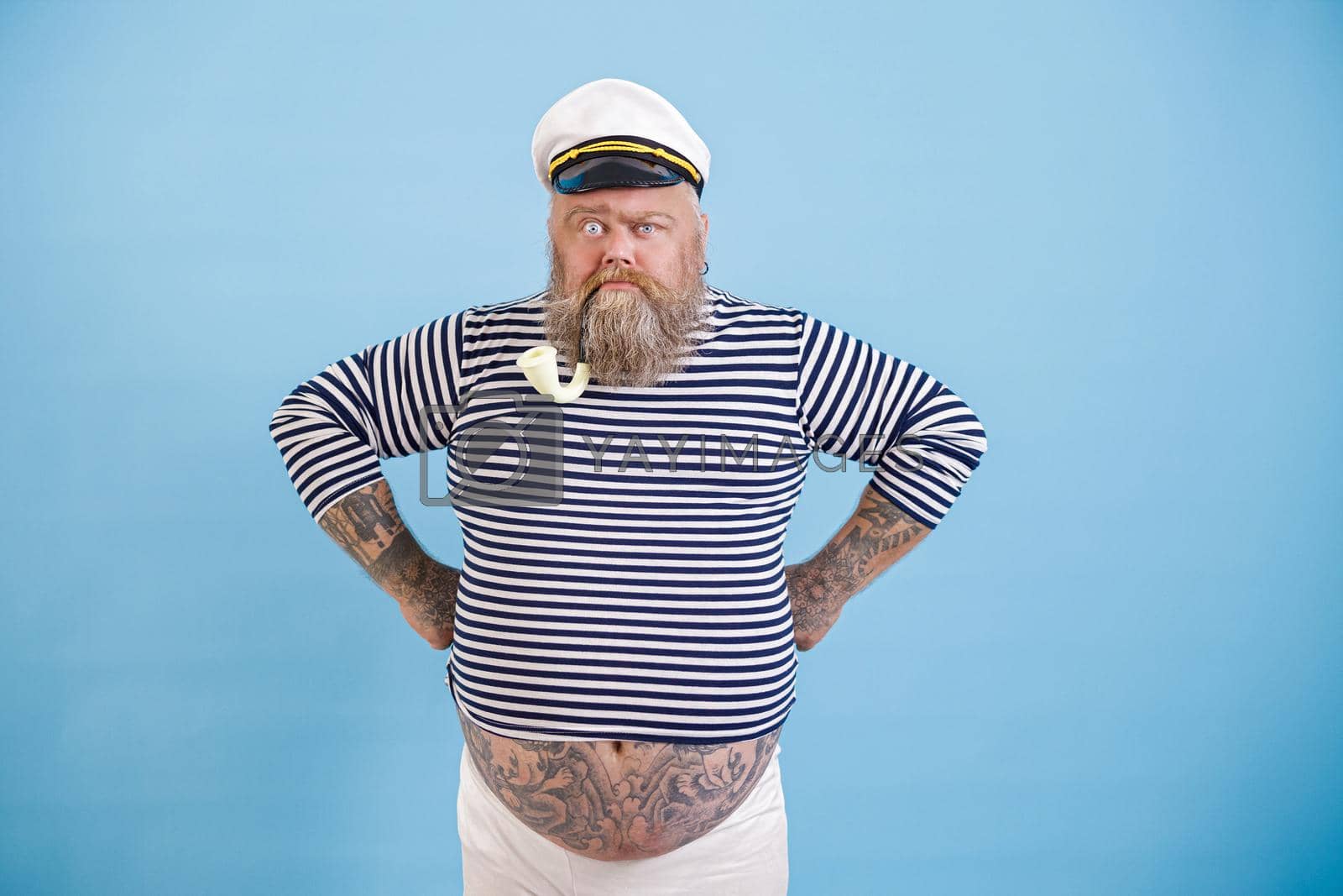 Royalty free image of Funny bearded fat man in sailor suit with smoking pipe on light blue background by Yaroslav_astakhov
