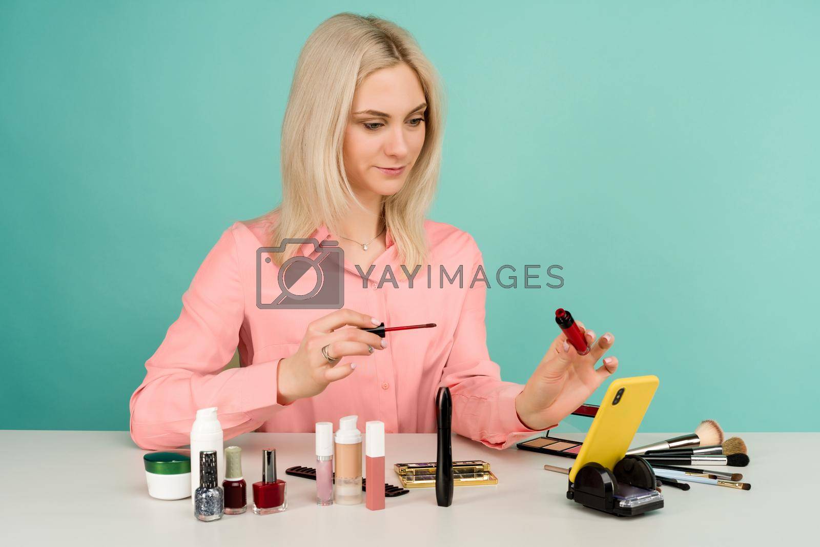 Candid shot of cute young Caucasian woman blogger presenting beauty products and broadcasting live video to social network, using lip gloss while recording everyday make up tutorial