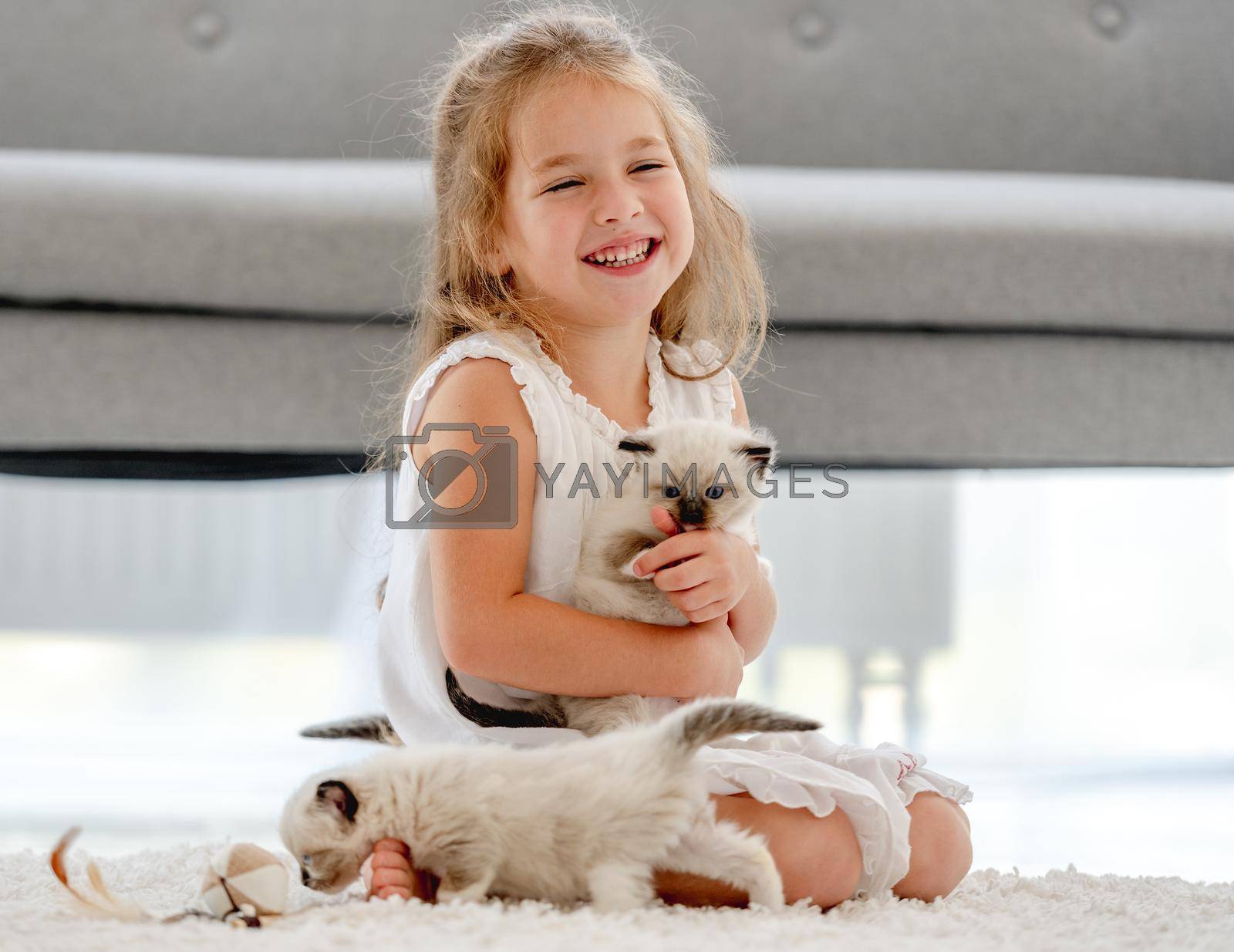 Child girl painting with ragdoll kittens on the floor and smiling. Little female person drawing with colorful pencils and kitty pets close to her at home