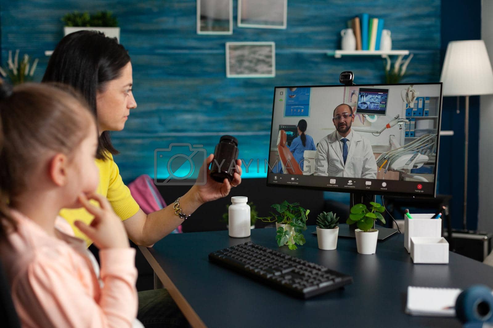 Mother discussing healthcare treatment with remote physician holding pills bottle in hands during online videocall meeting conference. Virtual consultation telemedicine on computer screen