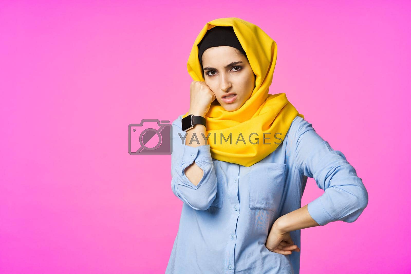 Royalty free image of cheerful woman in yellow hijab electronic watch technology user pink background by Vichizh