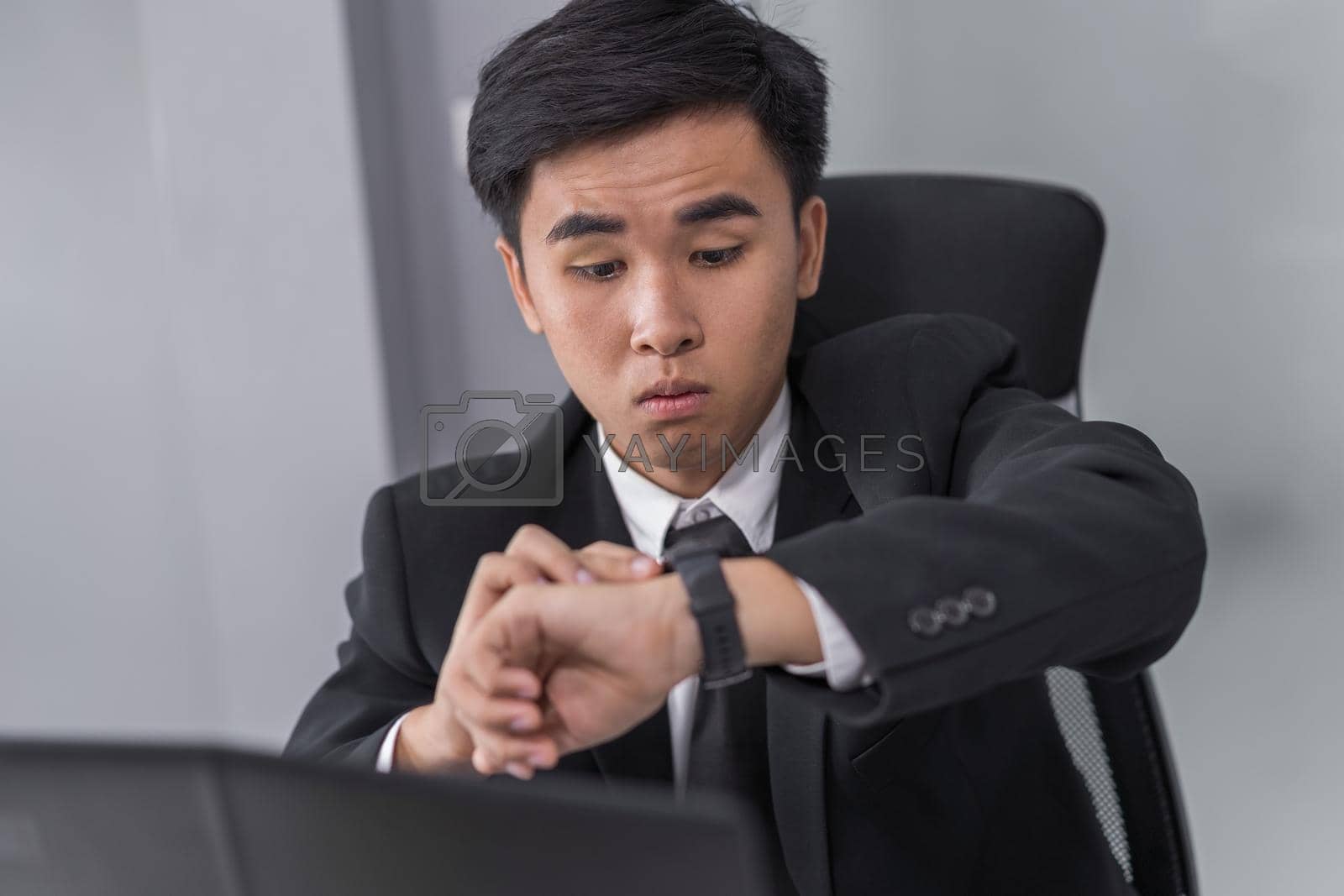 Royalty free image of business man checking time on watch while using laptop by geargodz